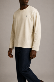 Side studio view of the TELLS Signature Sunfade Long Sleeve in Apricot, highlighting its boxy drape and long sleeves with dark indigo jeans.