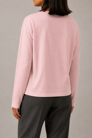 Plain back of the TELLS Quiet Sunfade Long Sleeve in Pink, showing the relaxed silhouette and open hem with charcoal trousers.