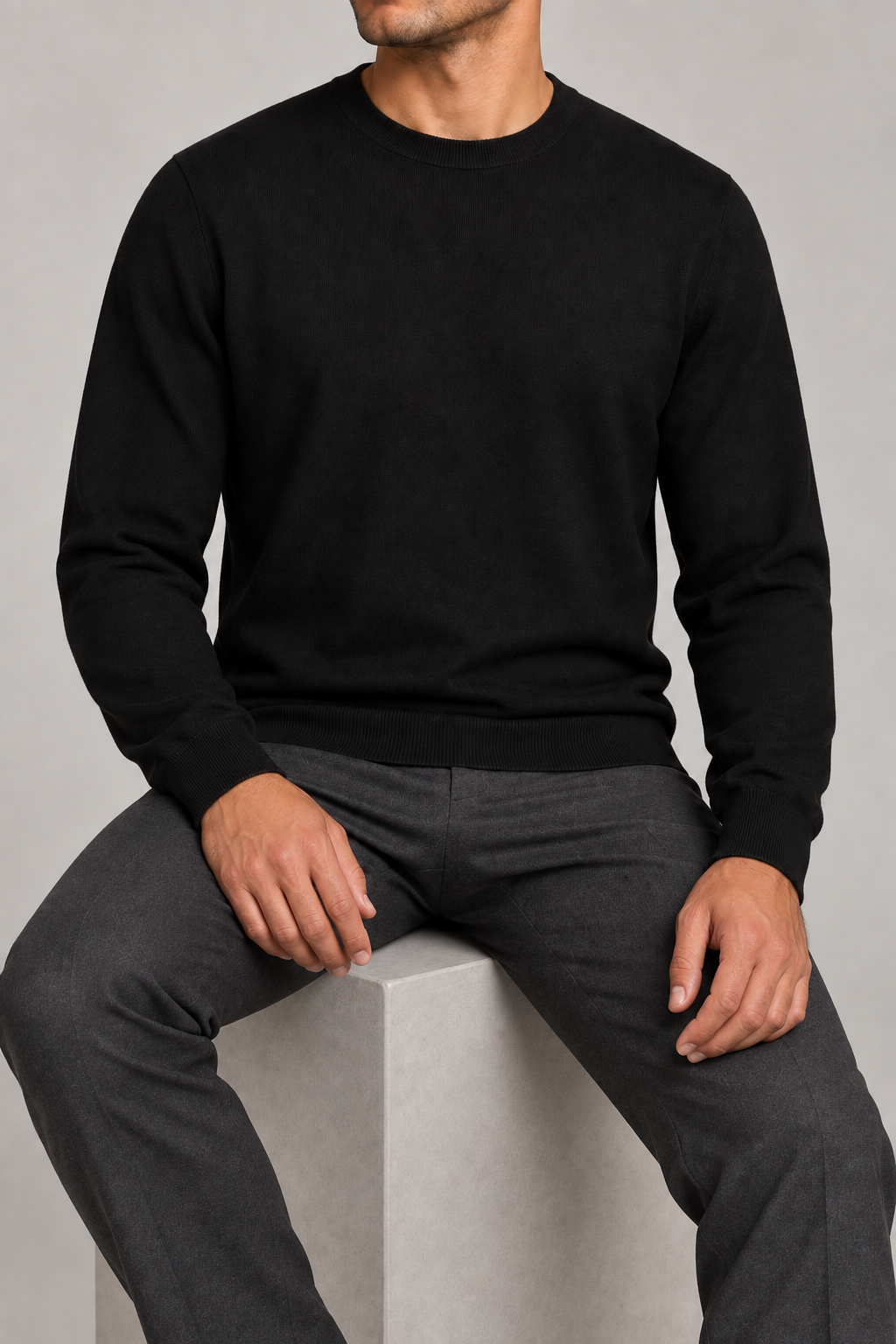 Seated studio view of Still Hours Crewneck Sweater in Black, showing the plain knit fabric draping naturally.