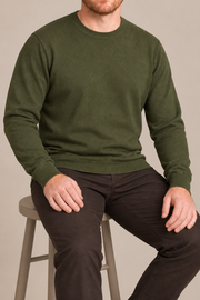 Seated studio view of Still Hours Crewneck Sweater in Olive, showing the natural drape of the plain knit.