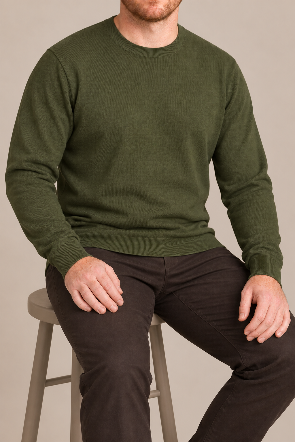 Seated studio view of Still Hours Crewneck Sweater in Olive, showing the natural drape of the plain knit.