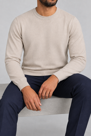 Seated studio view of Still Hours Crewneck Sweater in Sand, showing the natural drape of the plain knit.
