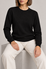 Seated studio view of Quiet Form Crewneck Sweater in Black, showing the natural knit drape.