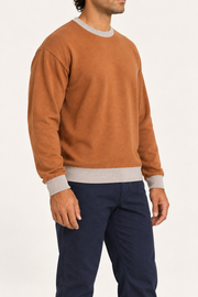 Slow Days Relaxed Crewneck in Rust with Coco Trim. Three-quarter view showing the relaxed shape and Coco cuffs and hem.