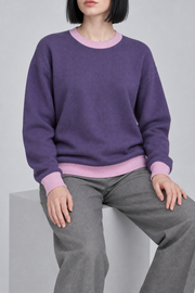 Soft Pause Relaxed Crewneck in Violet with Lilac Trim. Seated view showing the relaxed Violet knit drape and Lilac edges.