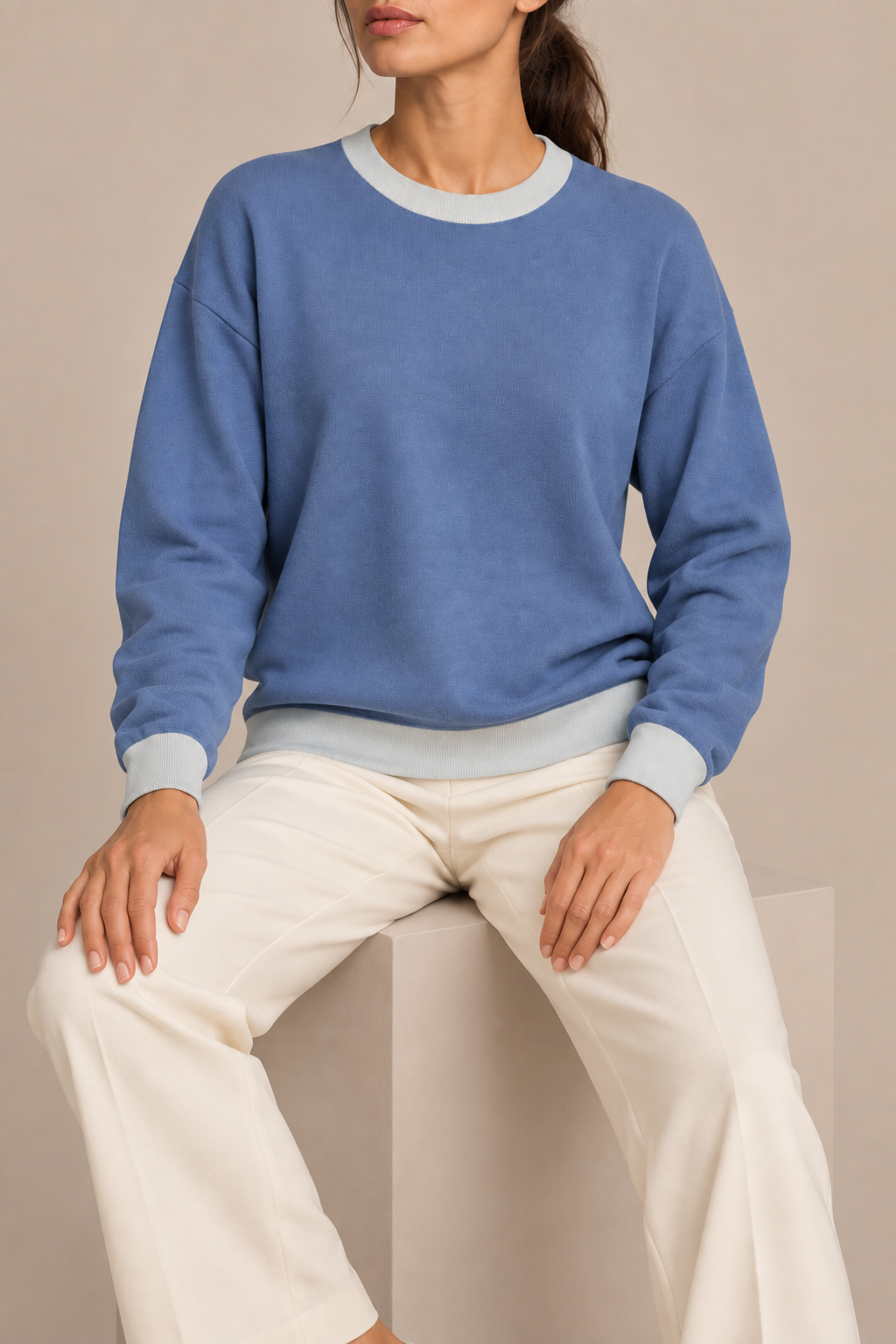 Soft Pause Relaxed Crewneck in Denim with Powder Trim. Seated view showing the relaxed Denim knit drape and Powder edges.