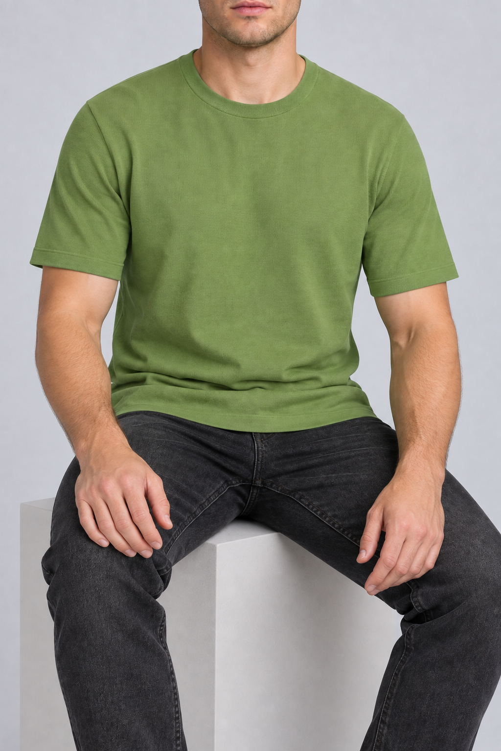 Seated studio view of Open Hours Knit T-Shirt in Grass, showing green knit drape above charcoal jeans.