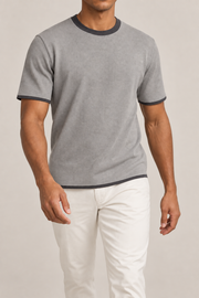 Walking studio view of Open Hours Knit T-Shirt in Grey with Charcoal Trim, showing grey knit drape above offwhite trousers.