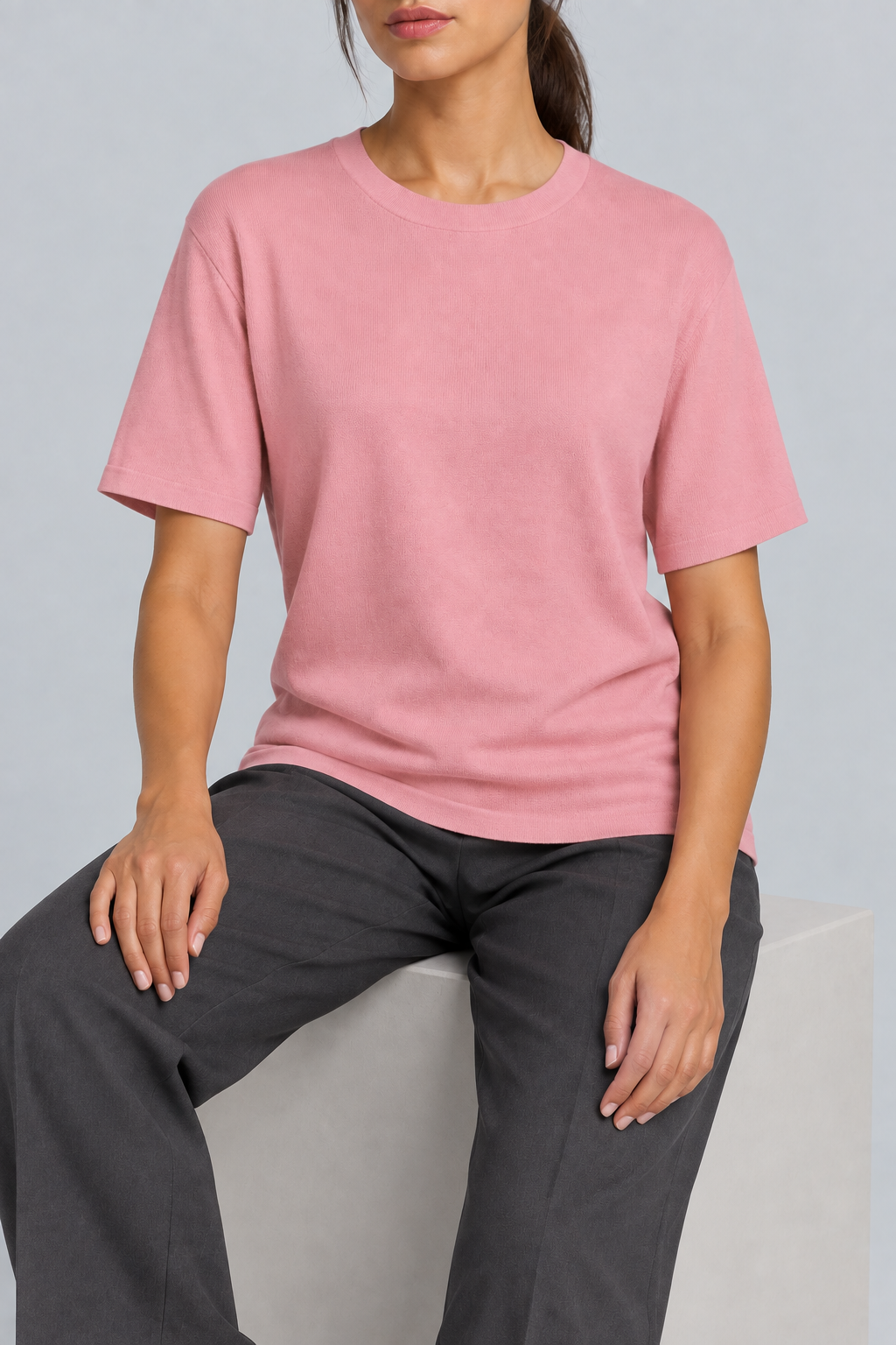 Seated studio view of Soft Tempo Knit T-Shirt in Pink, showing pink knit drape above charcoal trousers.