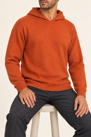Seated view showing the soft knit drape and long sleeves of Off Hours Knit Hoodie in Burnt Orange.
