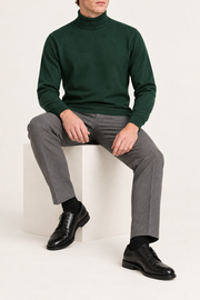 Seated view showing the Pine green knit drape and long sleeves of Still Season Turtleneck Sweater in Pine.