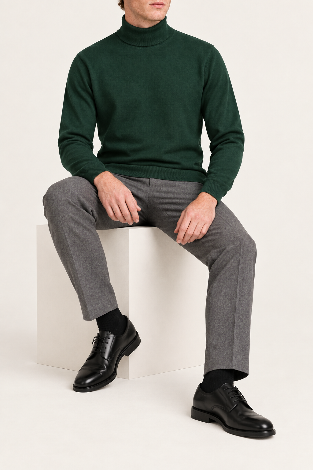 Seated view showing the Pine green knit drape and long sleeves of Still Season Turtleneck Sweater in Pine.