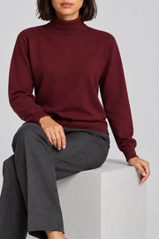 Seated view showing the Burgundy knit drape and long sleeves of Soft Horizon Turtleneck Sweater in Burgundy.