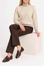 Seated view showing the Beige knit drape and Coco cuffs of Soft Horizon Turtleneck in Beige with Coco Trim.