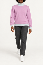Walking view showing the Lilac knit drape and Powder cuffs of Soft Horizon Turtleneck in Lilac with Powder Trim.