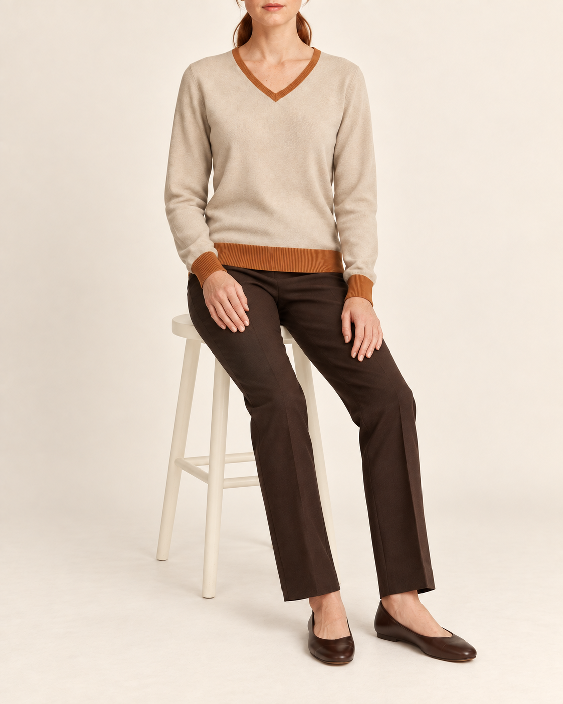 Seated view showing the Beige knit drape and Rust cuffs of Soft Angle V-Neck in Beige with Rust Trim.