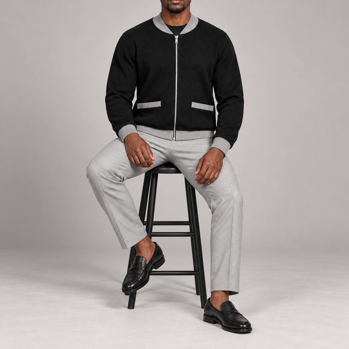 Seated studio view showing knit drape and grey-trimmed patch pockets of Afterlight Knit Bomber in Black with Grey Trim.