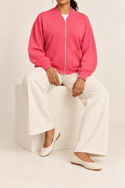 Seated studio view showing knit drape and front pockets of Soft Afterlight Knit Bomber in Hot Pink.
