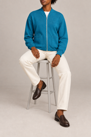 Seated studio view showing knit drape and front pockets of Soft Afterlight Knit Bomber in Cyan.