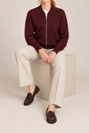 Seated studio view showing knit drape and front pockets of Soft Afterlight Knit Bomber in Burgundy.