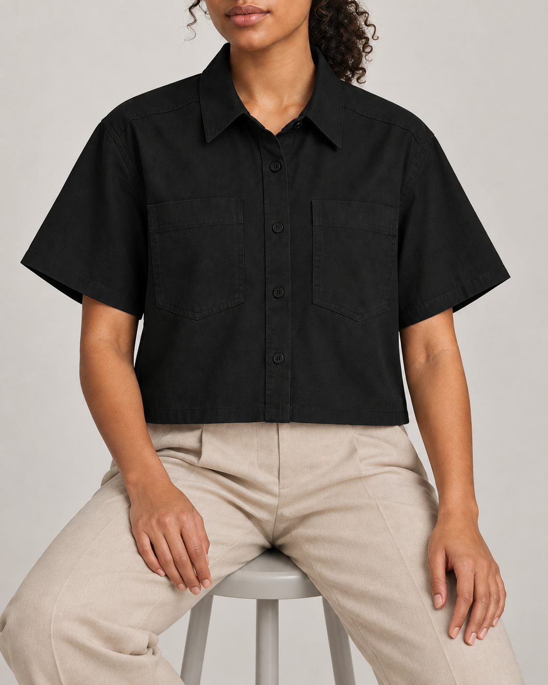 Seated view of Quiet Line Crop Shirt in Black, showing the relaxed drape and two patch pockets.