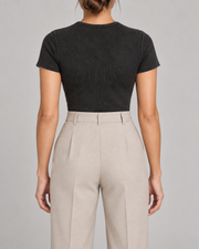 Rear studio view of Soft Trace Bodysuit in Washed Black, showing the plain high neckline and fitted back above beige trousers.