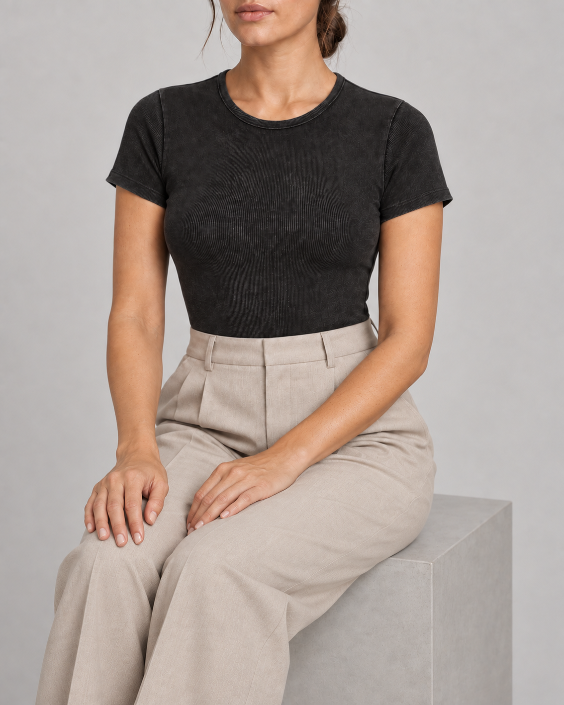 Seated studio view of Soft Trace Bodysuit in Washed Black, showing the close ribbed fit styled with beige trousers.