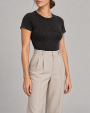 Three-quarter studio view of Soft Trace Bodysuit in Washed Black, showing the set-in sleeve and fitted side with beige trousers.