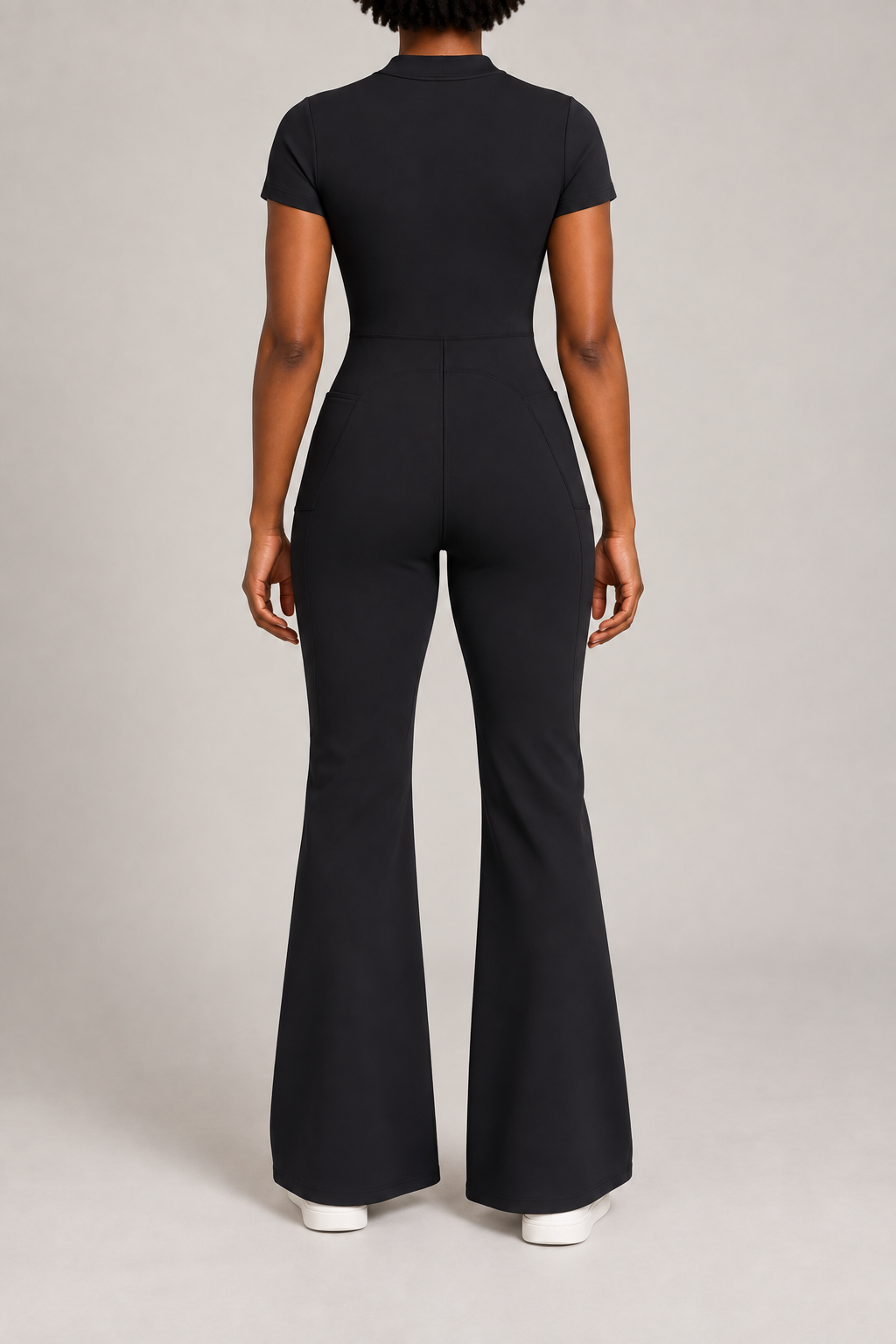 Contour Flare Zip Jumpsuit in Black. Rear studio view showing the back waist seam, curved shaping and plain finish.