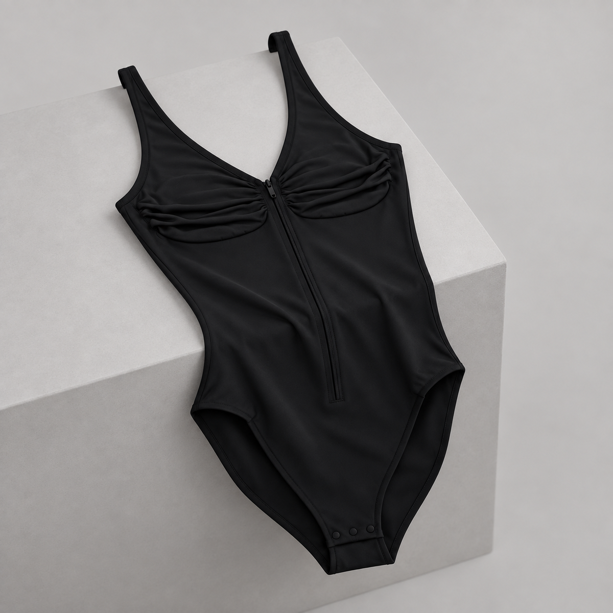 Soft Gather Zip Bodysuit in Black. Draped studio view over a gray block showing the ruched front and natural fabric folds.
