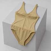 Soft Gather Zip Bodysuit in Khaki. Draped studio view over a gray block showing the gathered front and natural fabric folds.
