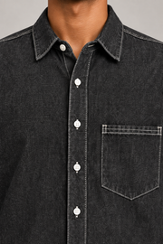 Close-up of Worn Line Denim Shirt in Black, showing the pointed collar, white buttons and contrast-stitched patch pocket.