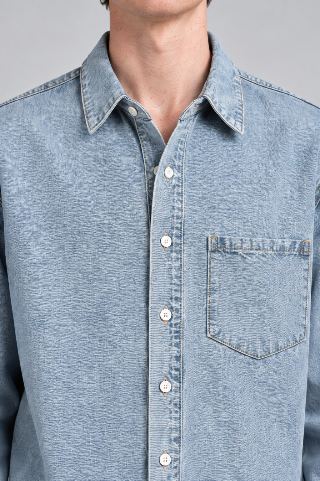 Detail view of Worn Line Denim Shirt in Blue, showing the pointed collar, tan stitching and white buttons on washed denim.
