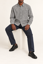Seated view of Worn Line Denim Shirt in Light Gray, showing the loose plain shape and natural drape over navy trousers.