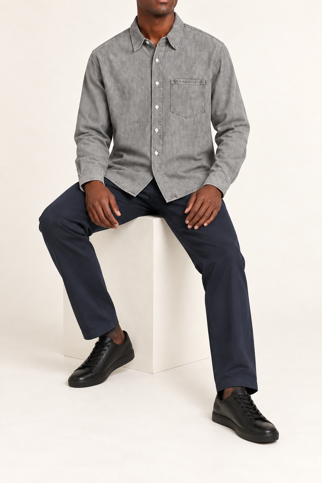 Seated view of Worn Line Denim Shirt in Light Gray, showing the loose plain shape and natural drape over navy trousers.