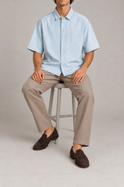 Seated view of Pale Current Lyocell Shirt in Light Blue, showing the loose plain shape and soft fabric drape.