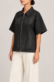 Three-quarter view of Soft Shift Zip Denim Shirt in Black, showing dropped shoulders, short sleeves and its plain boxy shape.