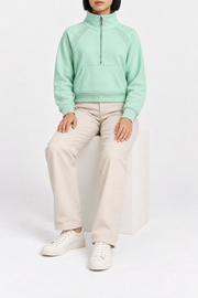Seated studio view showing the cropped shape and long raglan sleeves of Curve Interval Half-Zip Sweatshirt in Green.
