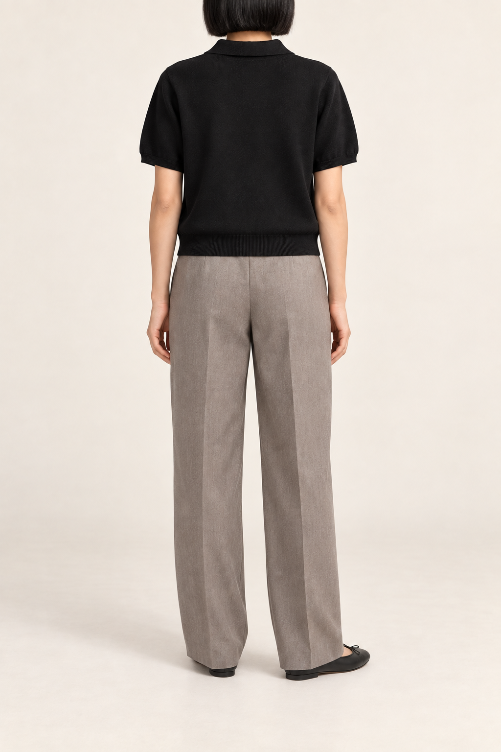 Soft Poise Knit Polo in Black. Rear studio view showing the plain black knit and ribbed hem.