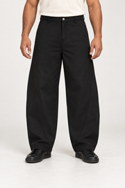 Front studio view of Quiet Arc Barrel Pants in Black, showing curved panel seams and a loose silhouette.