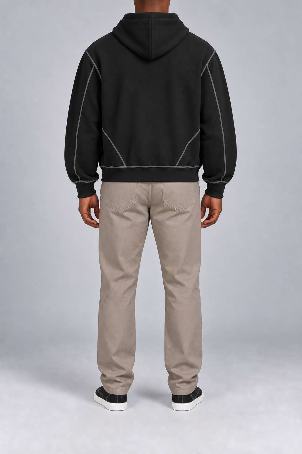 Rear view of Outline Studio Fleece Zip Hoodie in Black showing the plain hood and diagonal contrast seams near the hem.