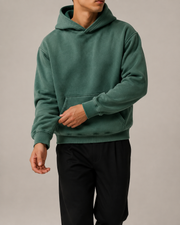 Front studio view of the TELLS Evergreen Washed Hoodie in Dark Green, styled with black trousers.