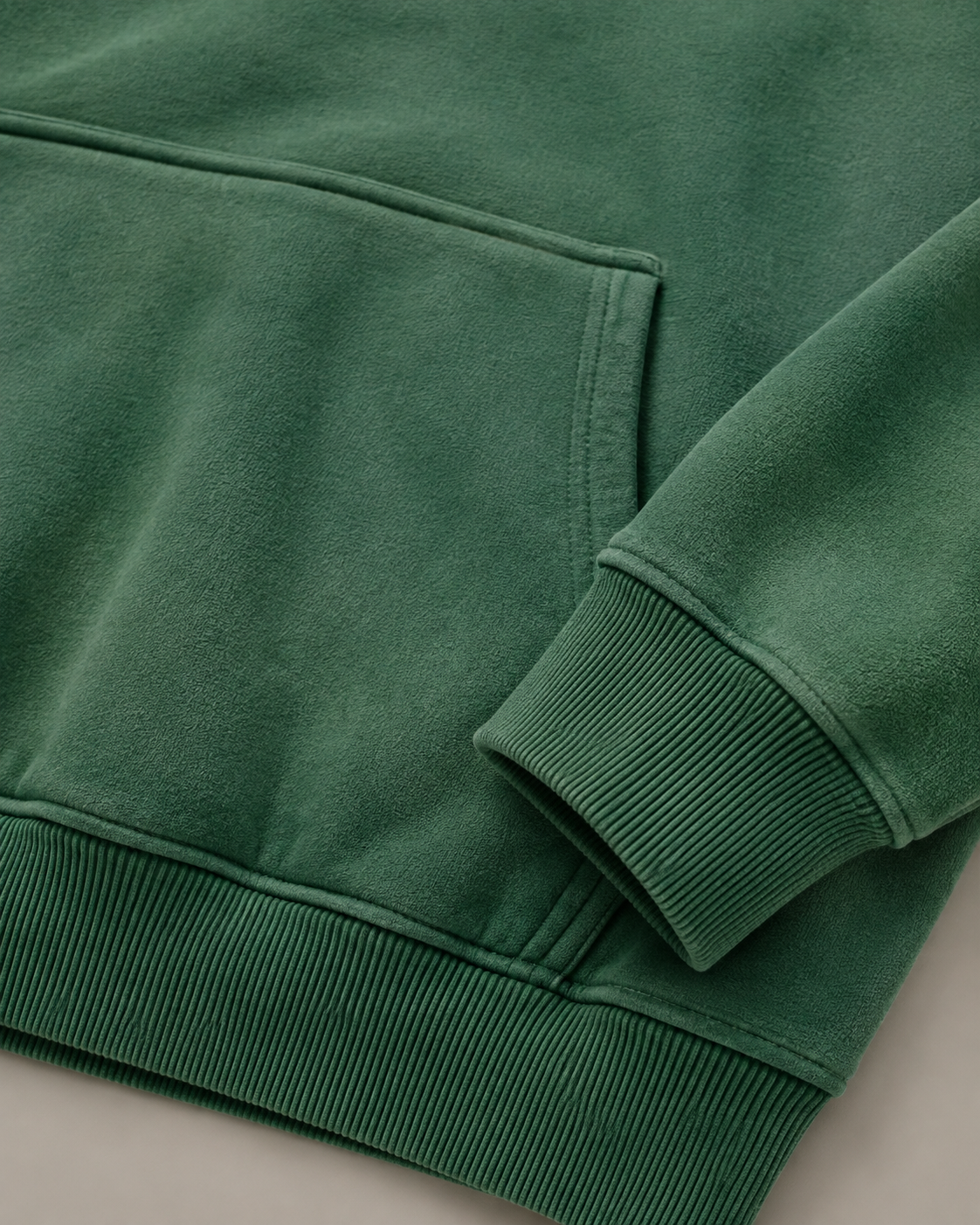 Studio close-up of the Dark Green Evergreen Hoodie, showing its washed texture, kangaroo pocket and ribbed cuff.